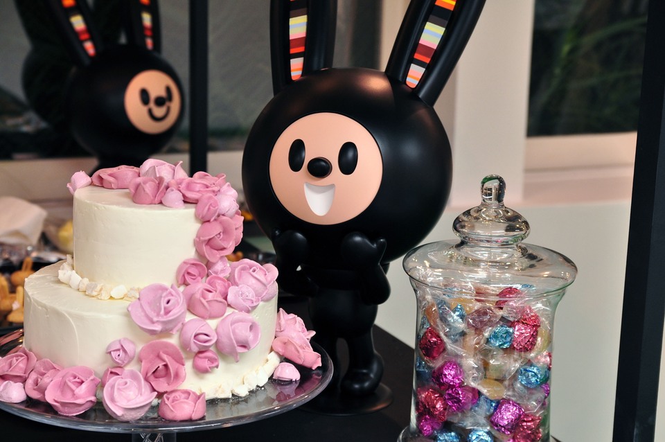 ストライプの耳を持つ黒いLUCKY BUNNY LUNNY（ラッキーバニーのラニー）の立体作品。隣にはピンクの花で飾られたケーキと、色とりどりのお菓子の入った瓶。